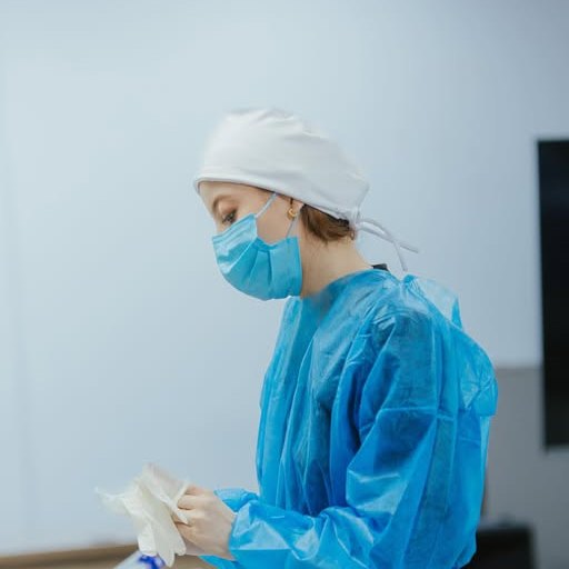 Dra. Emile Vitória de touca e avental azul durante atendimento na residência em Harmonização Orofacial
